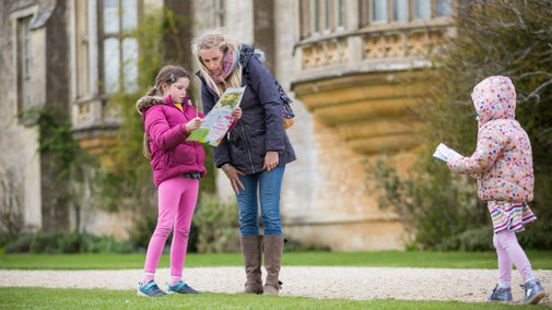 Woman and two young girls looking at trail sheets in grounds with Lacock Abbey in background